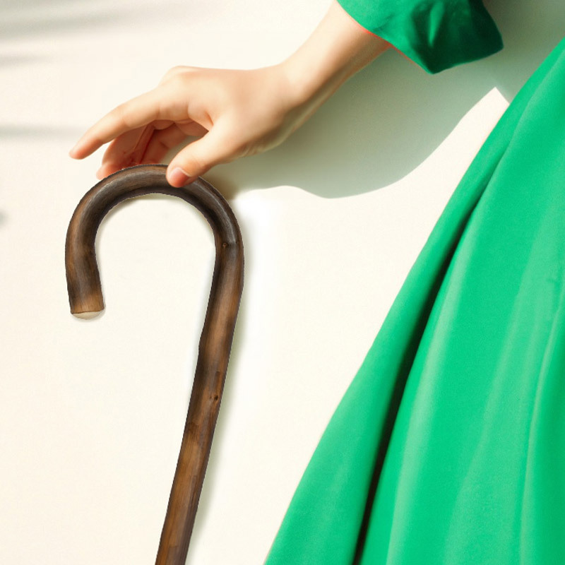 someone in a green dress holding a dark wood crook handle walking stick